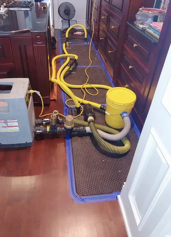 Drying mats and hoses on a wood floor beside kitchen cabinets