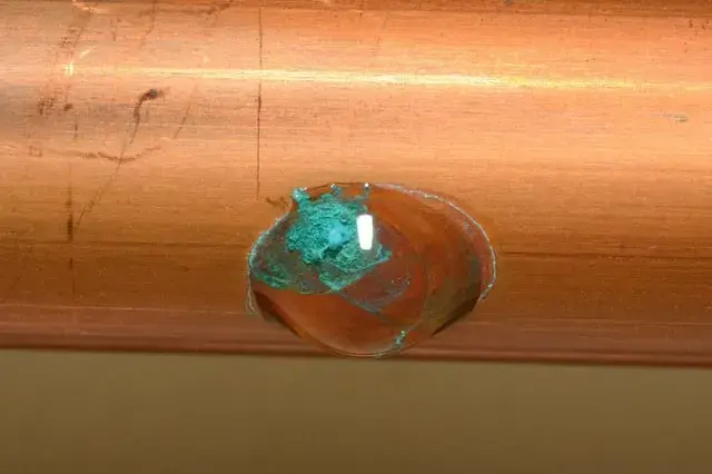 Close view of a pinhole in a copper pipe crusted with green corrosion