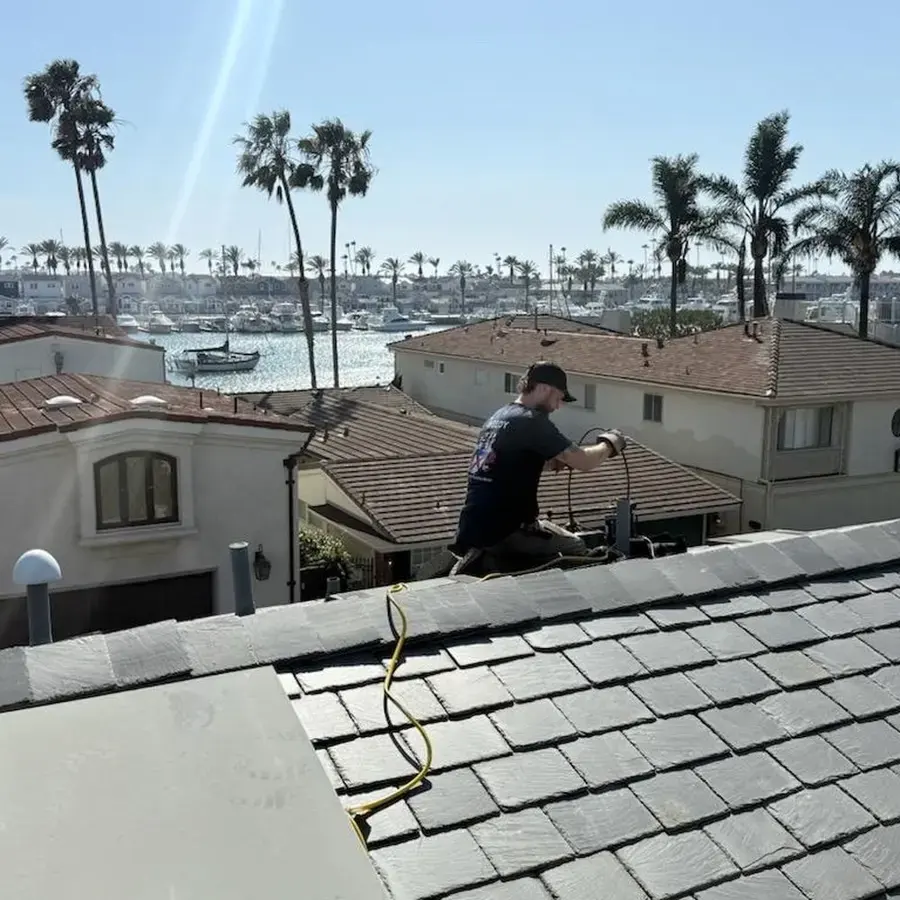 Technician checking a tile roof on a hillside home above the harbor and palm trees